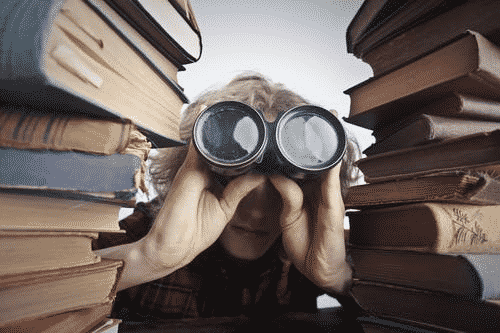 Boy with binoculars in between stacks of books