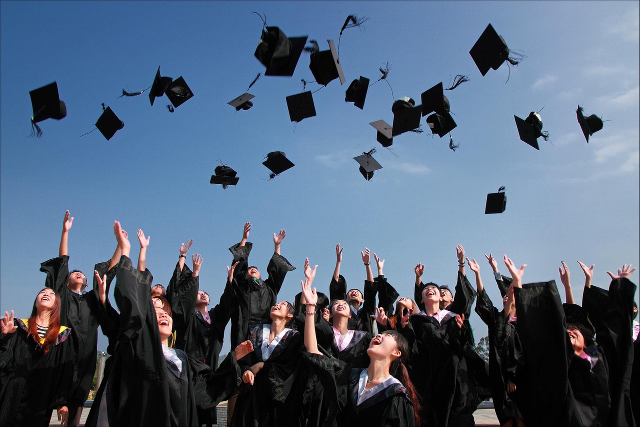 Newly Graduated People Wearing Black Academy Gowns Throwing Hats Up in the Air 