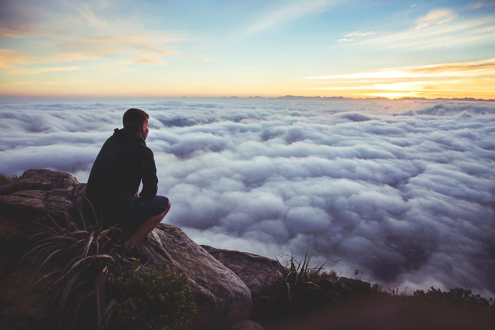 man sitting on mountain looking at clouds patience