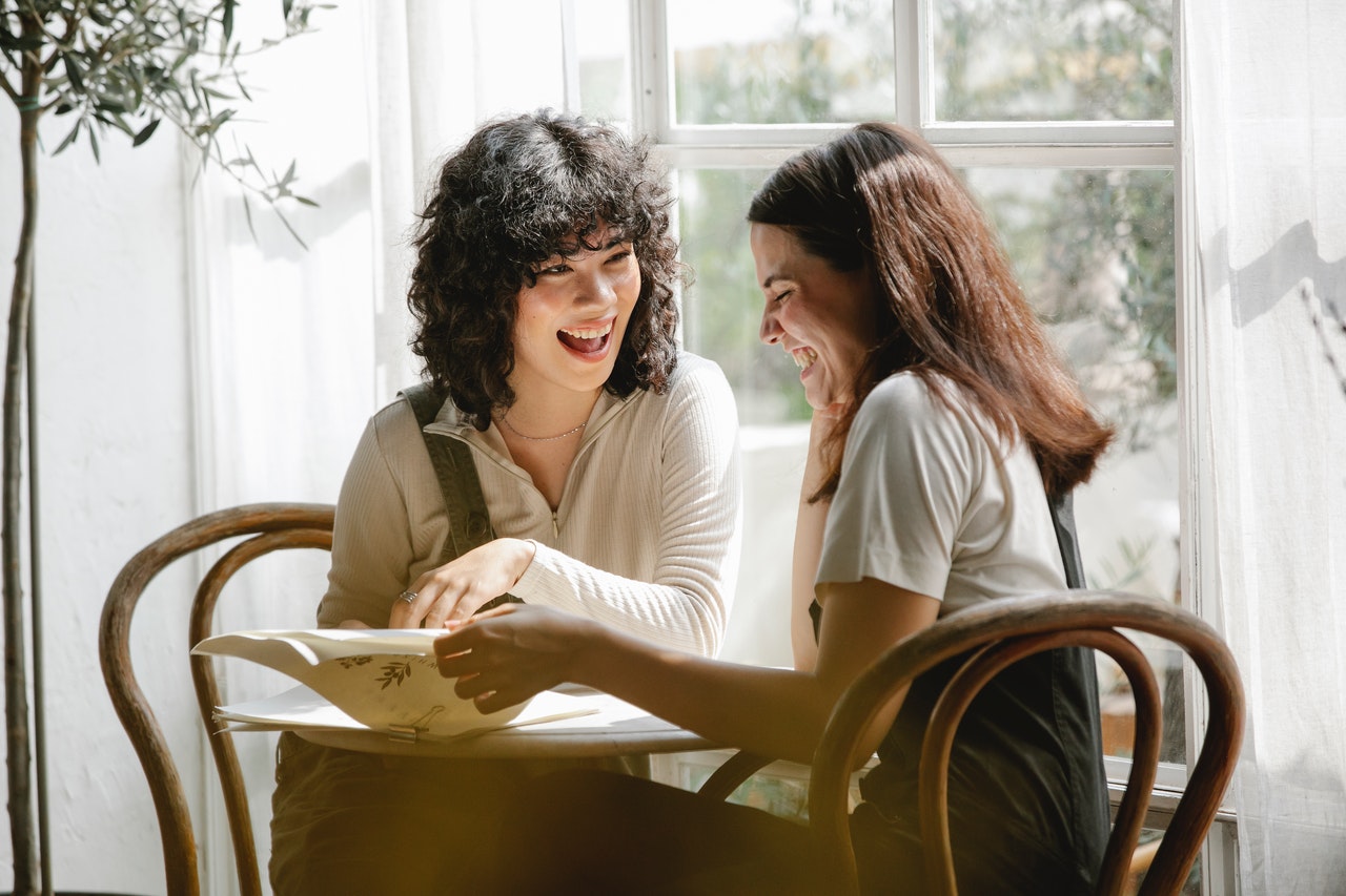 Cheerful diverse girlfriends reading document at table