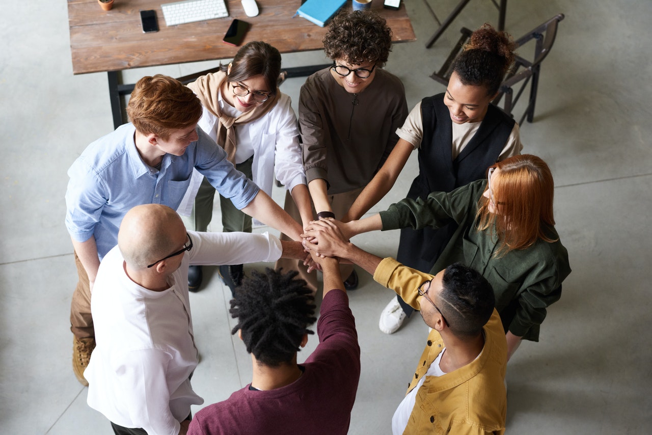 A group of young entrepreneurs around a table putting their hands together in unity. 